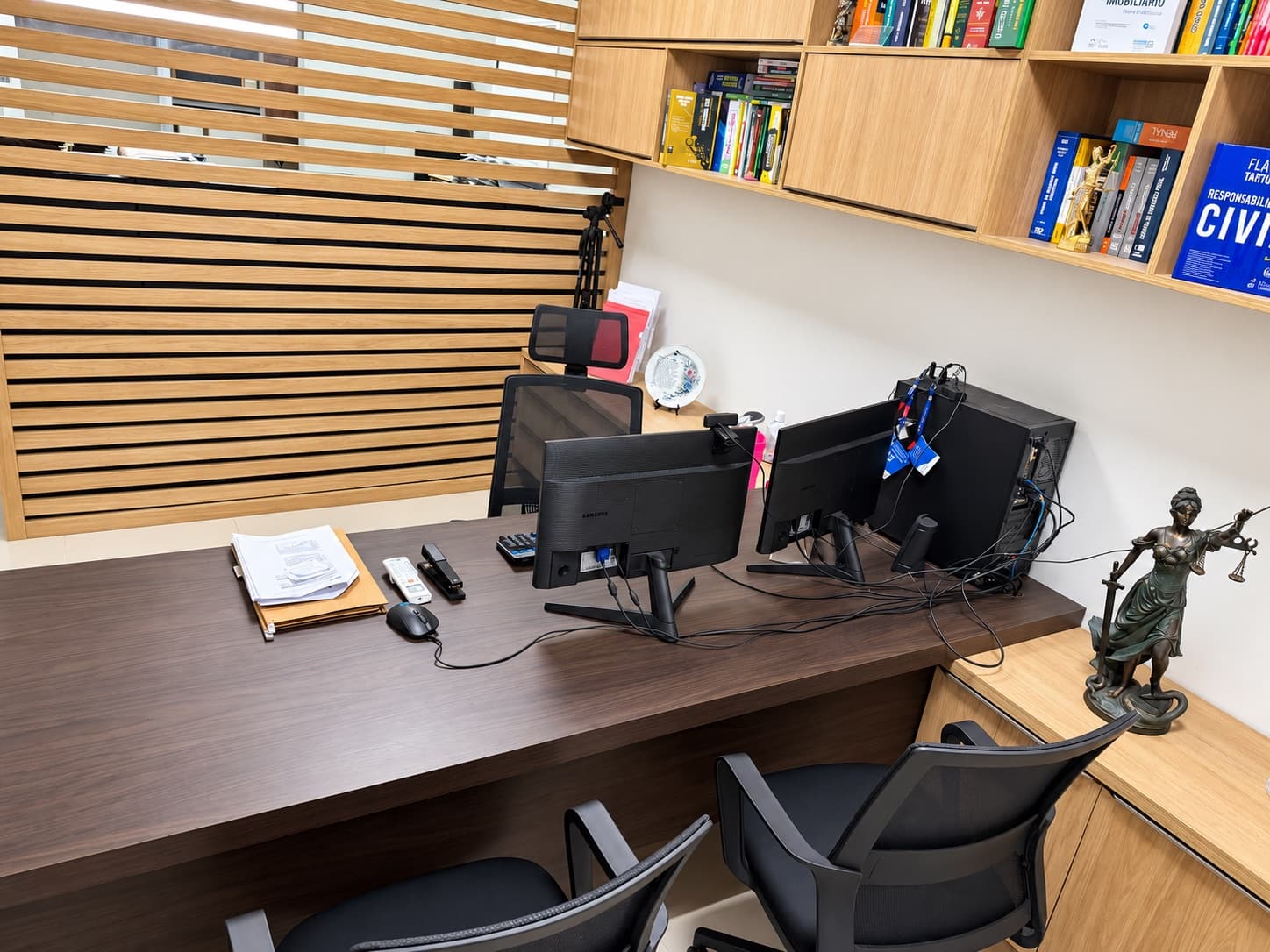 Mesa de atendimento com monitores e biblioteca jurídica ao fundo